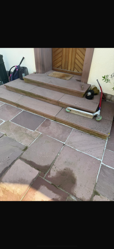 Drei Holzstufen führen zu einer Tür, daneben liegt ein Werkzeug und ein E-Scooter.